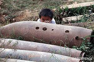 Niño en Laos jugando junto a una bomba de racimo.